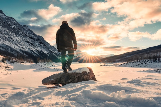 Solo young adventurer standing on snow covered lake with sunrise over Medicine Lake in morning on winter at Jasper national park