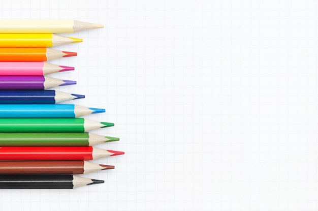 Solored pencils in a wave on the background of a sheet of a notebook