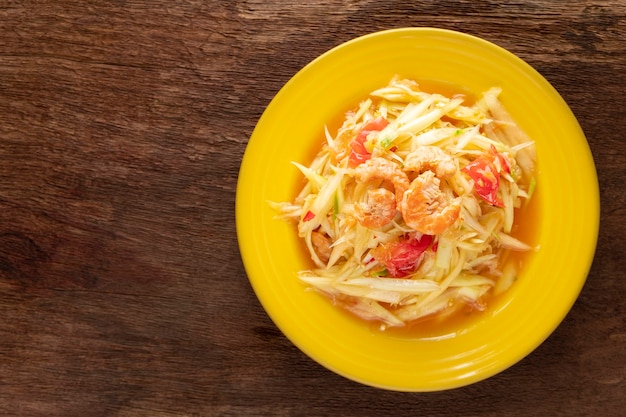 Som Tum Thai, Som Tam Thai, Thai food, spicy papaya salad with, tomato, lime and chilli topping with dried shrimp on natural wood texture background, top view