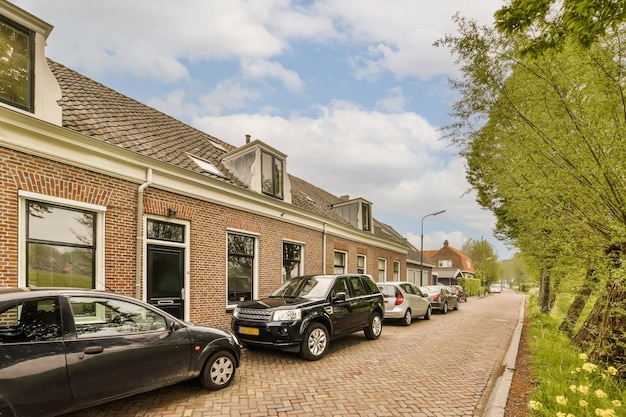 some cars parked on the side of a street in front of a brick building with green trees and yellow flowers