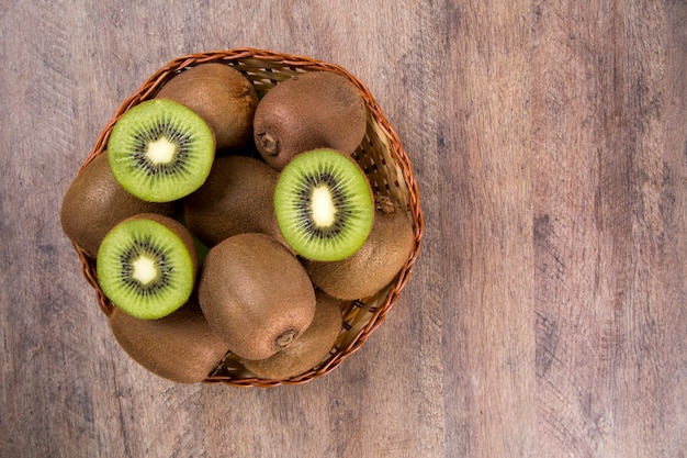 Some kiwis in a basket over a wooden surface. Fresh fruits