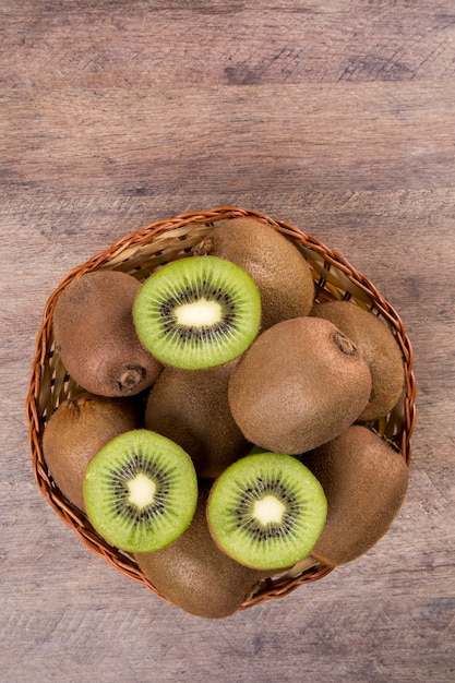 Some kiwis in a basket over a wooden surface. Fresh fruits