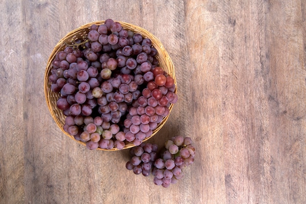 Some red grapes in a wooden pot over a wooden surface seen from above