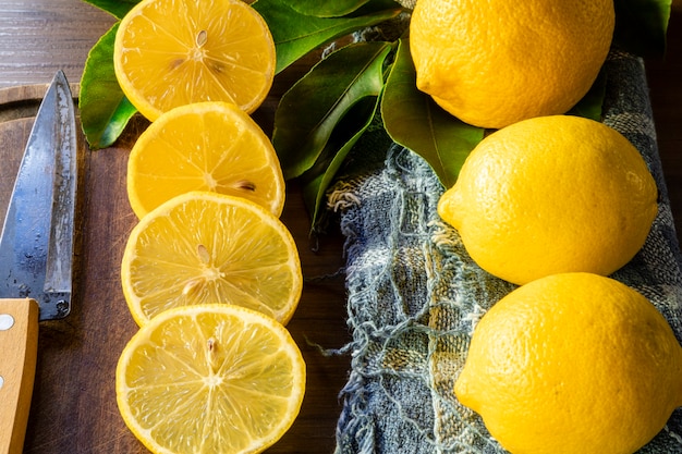 Some slices of lemon cut on a wooden board next to a knife on a rustic background