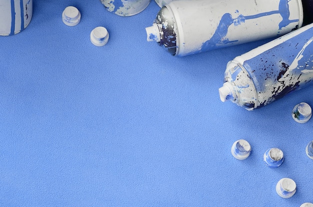 Some used blue aerosol spray cans and nozzles with paint drips lies 