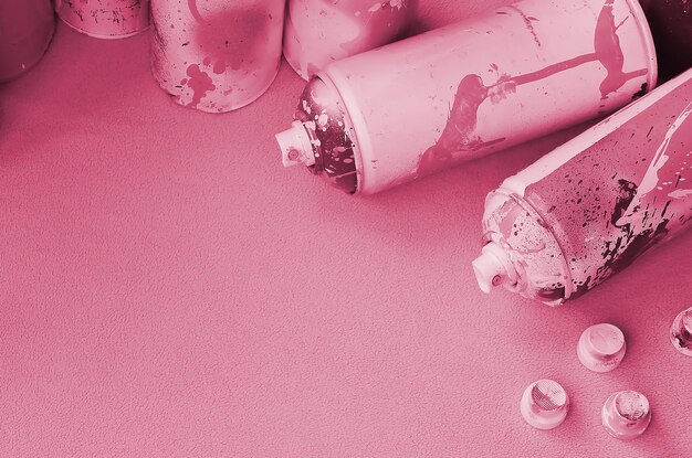 Some used pink aerosol spray cans and nozzles with paint drips lies on a blanket of soft and furry light pink fleece fabric Image toned in Viva Magenta color of the year