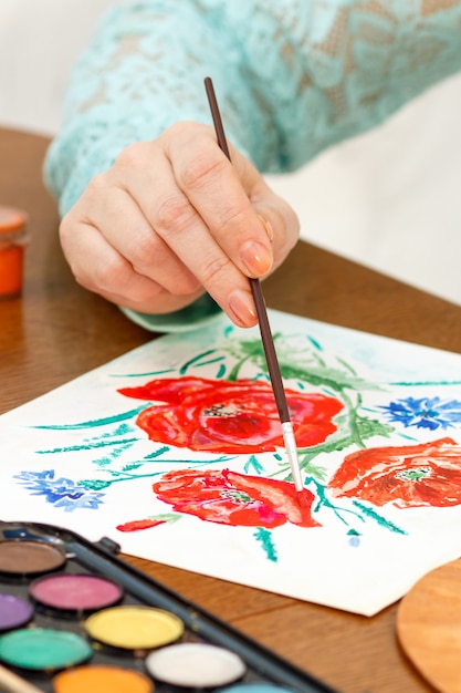 Someone painting poppy flowers on a white sheet of paper