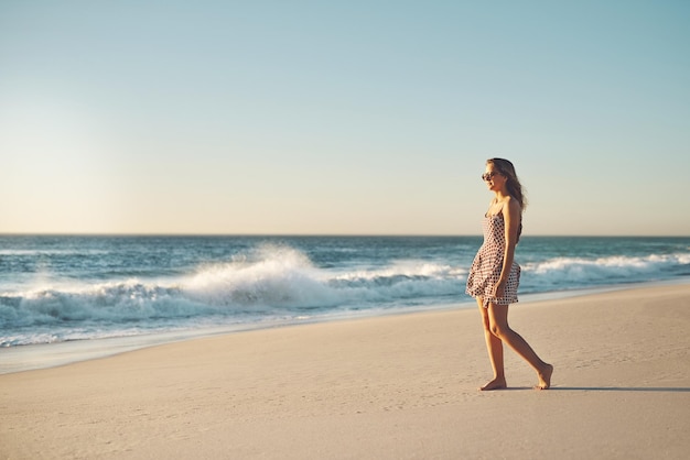 Sometimes the beach is all you need Shot of a young woman taking a stroll on the beach