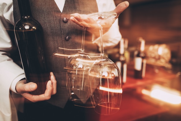 Sommelier in bow tie is holding with bottle and glasses