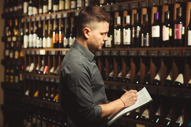 Sommelier male putting down information about wine products standing in cellar