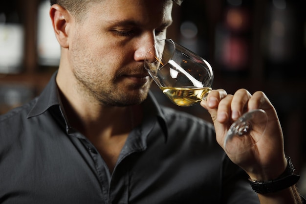 Sommelier smelling flavor of white wine in bokal on background of shelves with bottles in cellar