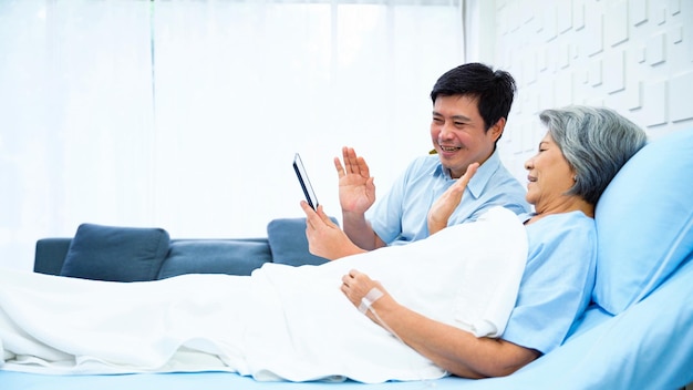 Son of an elderly woman patient Using a tablet to record a video while mom is lying in bed