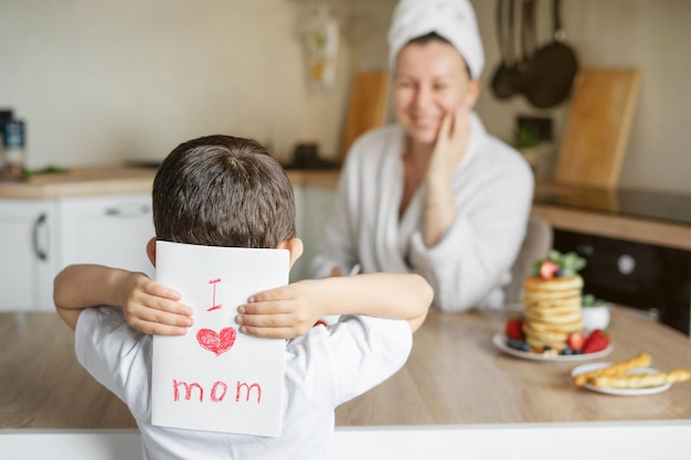 The son gives his mother a card with mother's day Breakfast surprise from a child Hands on the table with pancakes take a card