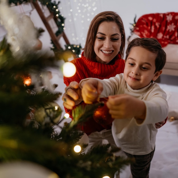 Son helping his mother in decorating Christmas tree fir making wish waiting for miracle at home