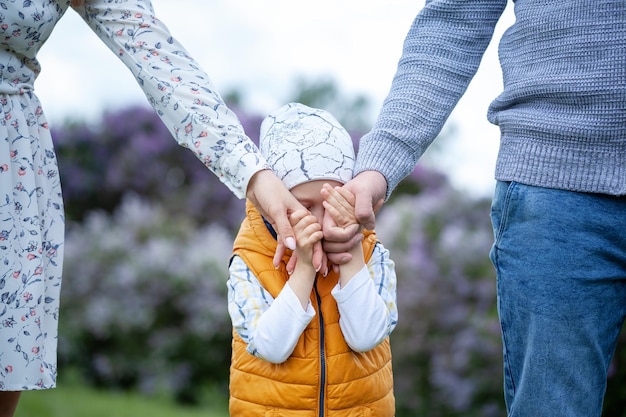 Son holding mother and father for hands. Child covers his face with his hands, hides.