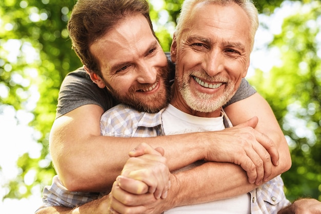 Son Hugs Old Man. Family Walking in Park Together.