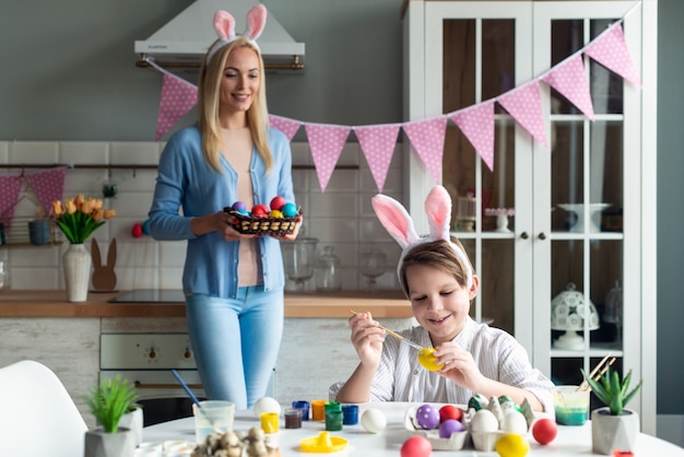 Son is painting Easter eggs, mom is watching and holding a basket.