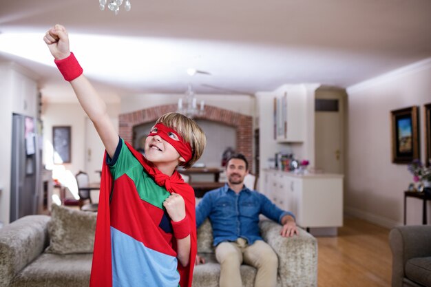 Son pretending to be a superhero while father sitting on sofa