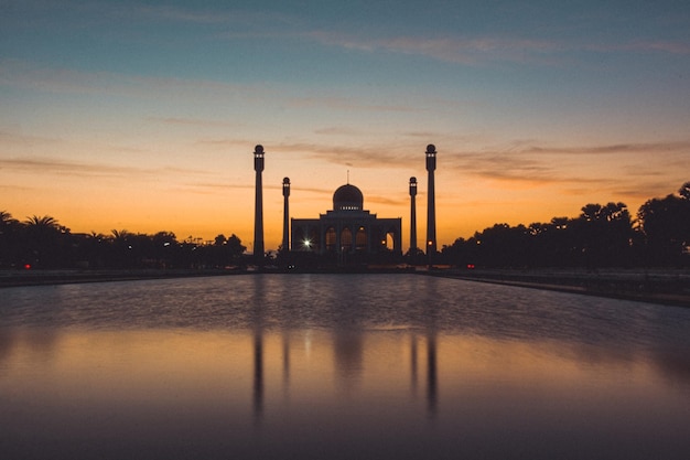 Songkhla Central Mosque in day to night with colorful skies at sunset and the lights of the mosque and reflections in the water in landmark landscape concept