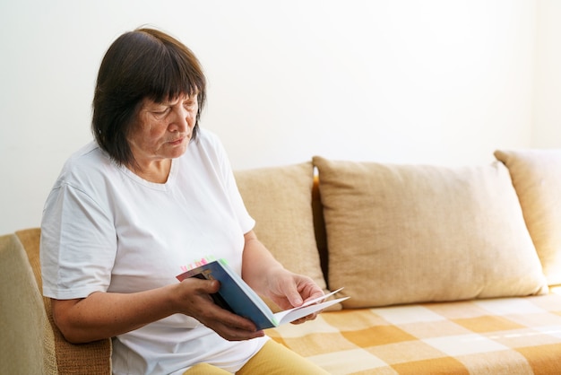 Soothing reading portrait of thoughtful elderly woman reading her favorite literature in cozy home s...