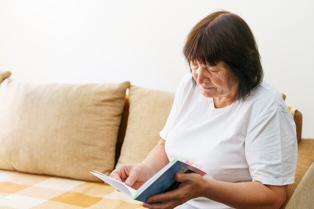 Soothing reading portrait of thoughtful elderly woman reading her favorite literature in cozy home s...