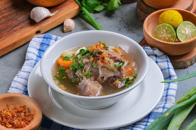 Sop buntut or oxtail soup is served in white bowl on rustic grey background. indonesian traditional culinary