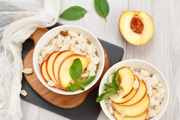 Sorghum porridge with pieces of peach cashew nuts and almond in porcelain bowls fresh peaches