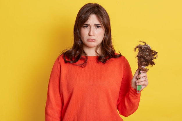 Sorrowful girl with purse lips showing to front comb with her lost hair