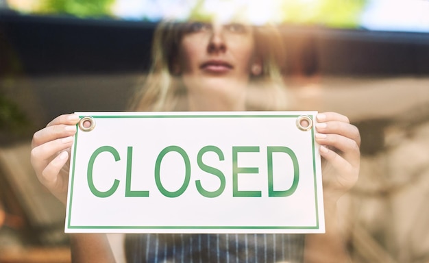 Sorry were closed Shot of a woman putting up a closed sign in a bar