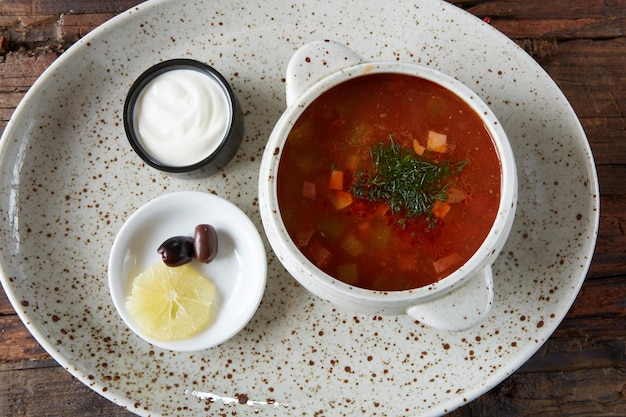 Soup saltwort with lemon meat pickles tomato sauce olives in a bowl on a sacking