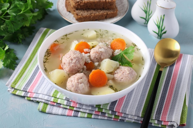 Soup with chicken meatballs rice and vegetables in a white bowl on a blue background Closeup