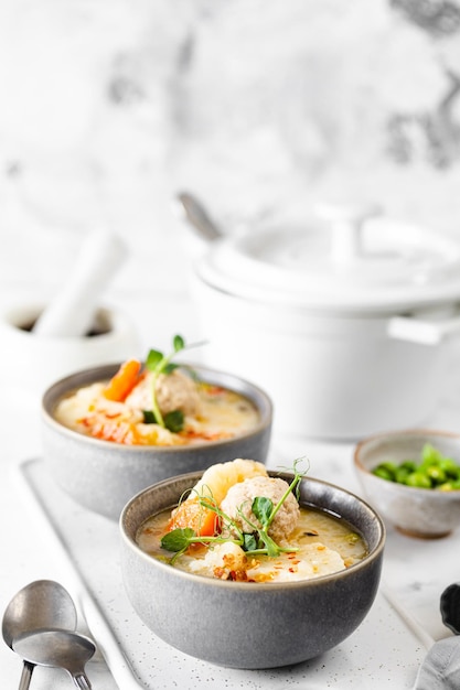 Soup with chicken meatballs and spring vegetables on a white background Vertical