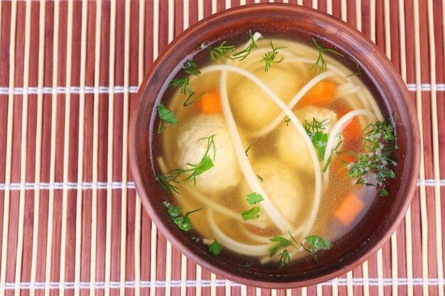 Soup with meatballs and noodles in bowl on bamboo mat background