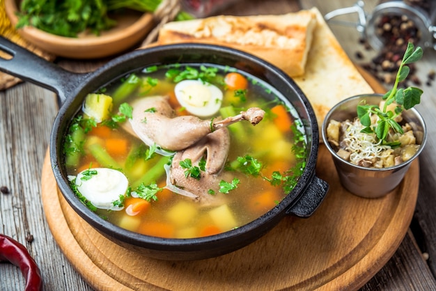 Soup with quail meat, with quail eggs and vegetables, in a frying pan