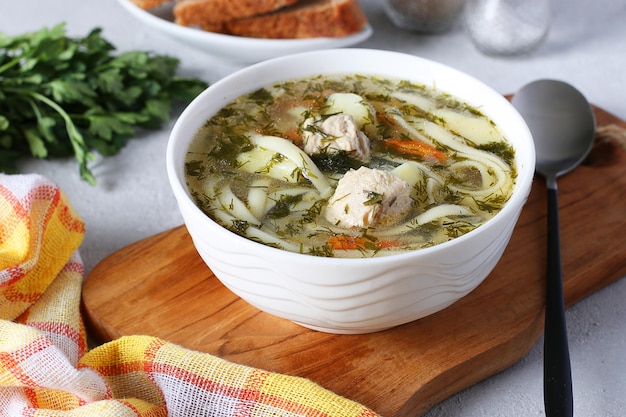 Soup with turkey noodles and vegetables in a white bowl on a wooden board