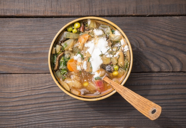 Soup with vegetables and sour cream in a deep plate on the surface of the dark boards. Top view.