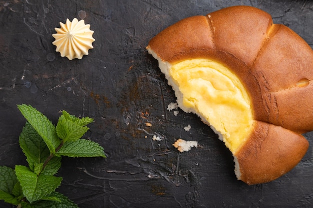 Sour cream bun with cup of coffee on a black concrete background and linen textile. top view, flat lay, close up.