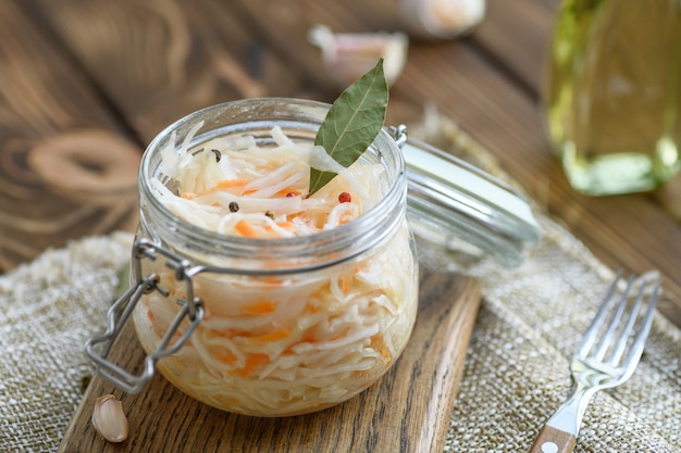 Sour, pickled sauerkraut with carrots and bay leaves in a glass jar.