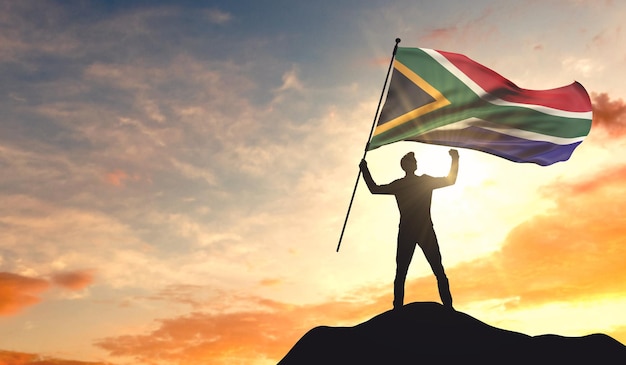 South Africa flag being waved by a man celebrating success at the top of a mountain 3D Rendering