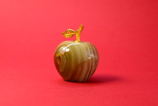 Souvenir from onyx or marble miniature apple figure with golden branch and leaf on red background