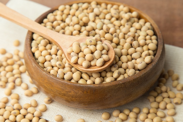 Soybeans in wooden bowl and spoon putting on linen and wooden background.