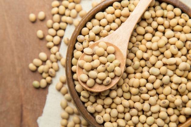 Soybeans in wooden bowl and spoon putting on linen and wooden background.