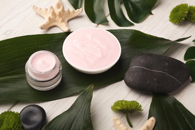 Spa background. Natural sea salt with essential oisl and various cosmetology products on green leaves background. Salon or home body and skin care