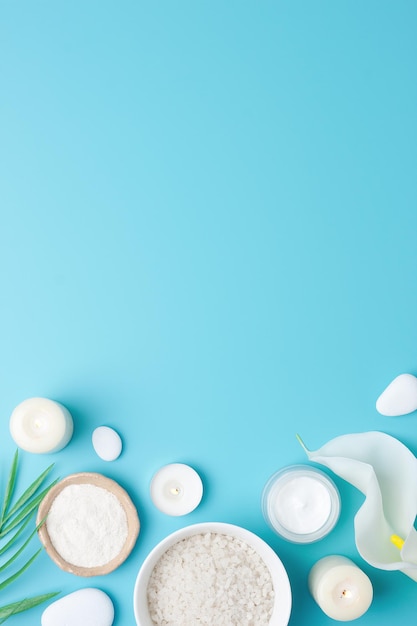 Photo spa background with bowl of salt skin care products white stones candles palm leaf and white flower on blue flat lay copy space