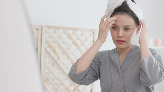 Over a spa background a young gorgeous woman with a towel on her head cheerfully touches her cleaned facexA