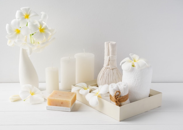 Spa composition massage hearbel ball,plumeria flower in vase,coconut coffee soap,white towels and candle on white wood table background,soft white tone still life