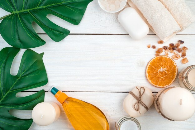 Spa composition with citrus oil, candles with care products on a white background with monstera leaves. Top view with copy space.