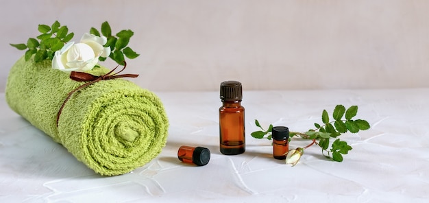 Spa composition with glass vial with essential oil, rolled towel and rose flower