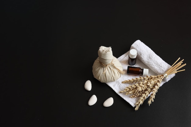 Spa composition with herbal massage bag, wheat sprig, oils and loofah on black background, copy space.