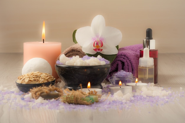 Spa composition with orchid flower, bowl with sea salt, bottles with aromatic oil, soap, scrub, candles and towels on wooden board